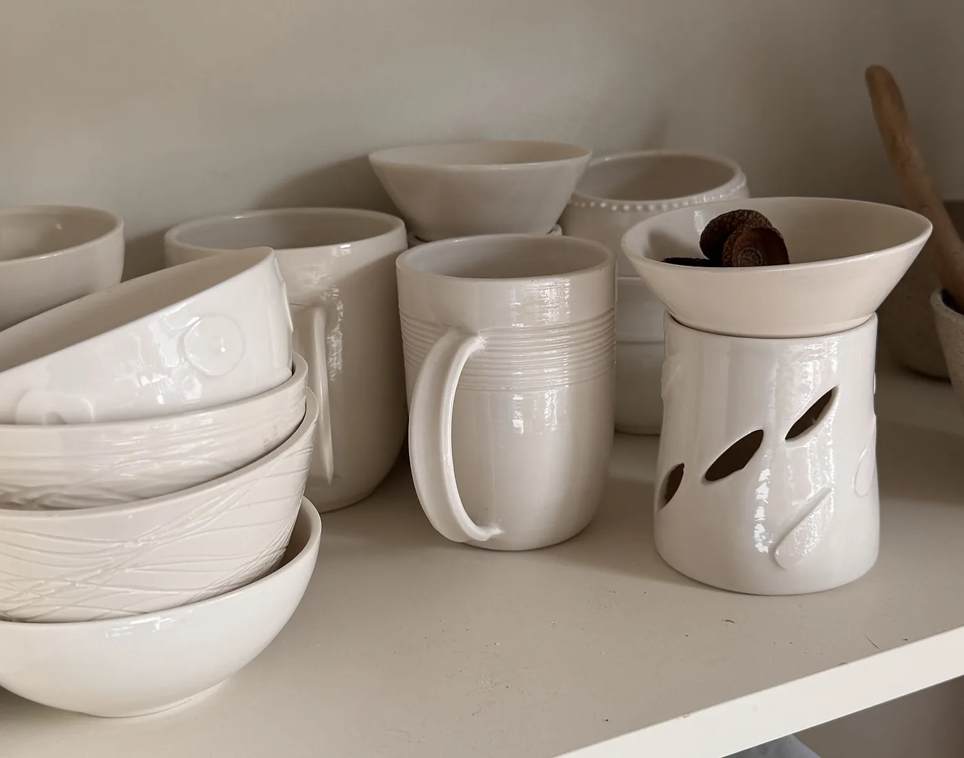 Weiss glasierte Schalen, Becher und Duftlampe im Regal