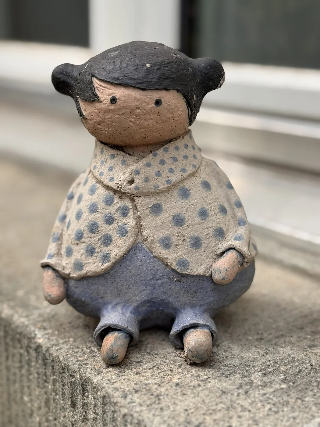 Sitzende Figur mit gepunkteter Jacke und blauer Hose